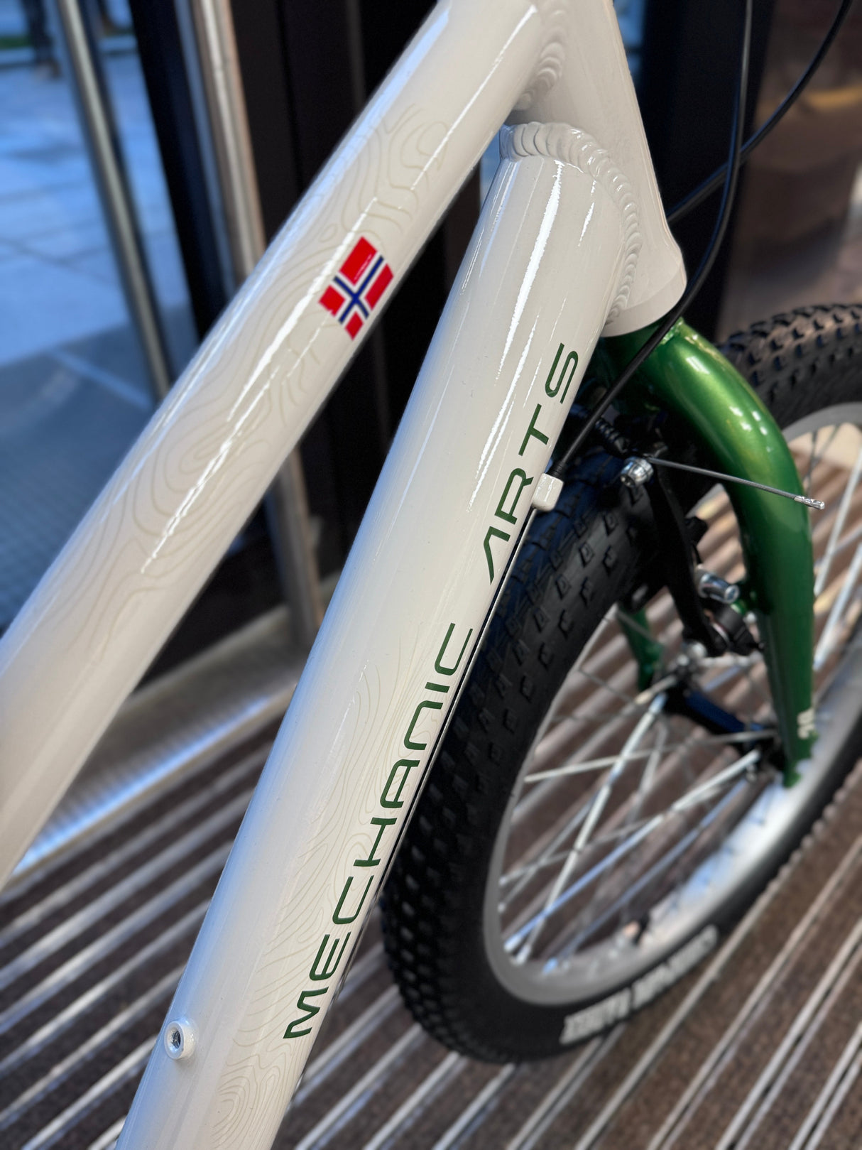 Nærbilde av Mechanic Arts-logo på Raskr barnesykkel ramme – vertikal tekst på kremhvit down tube med norsk flagg, premium finish og kvalitetslakk