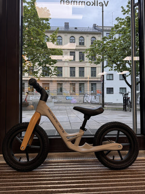 Beige balanse sykkel for barn fra Mechanic Arts Trillr, vist i butikkvindu fra siden – en stilig barnesykkel uten pedaler