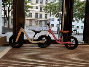 To Mechanic Arts Trillr barnesykler i beige og rosa side om side i butikkvindu – søte balanse sykler for søsken eller venner
