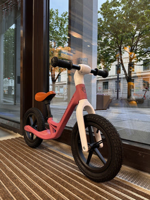 Forfra vinklet sidevisning av rosa Mechanic Arts Trillr balanse sykkel – moderne barnesykkel med grovt dekk for stabilitet i butikkvindu